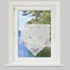 A white lace curtain with purple butterfly embroidery hangs in a window, with a view of trees and water outside. Anteprima dell’immagine prodotto