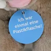 A close-up of a blue tag attached to a stuffed animal. Produktbild-Vorschau