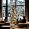 A family sits in a living room looking out a large window at a snowy forest scene with a decorated Christmas tree. Produktbild-Vorschau