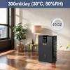 A black dehumidifier is shown in a well-lit room with a plant and a lamp. Náhled obrázku produktu