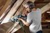 A man is using a reciprocating saw to cut through wooden beams in an attic or similar structure. Voir les images du produit
