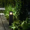 A black LED garden light is illuminated at night, surrounded by lush green plants and a wooden deck. Anteprima dell’immagine prodotto