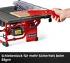 A hand is holding a red push stick to guide a piece of wood through a table saw. The table saw is red and black with a clear blade guard. Náhľad obrázku produktu