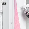 A close-up of a person's hand holding a spray can, applying sealant to a window frame. A pink sealing tape is visible. Produktbild-Vorschau