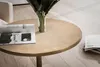 A round golden coffee table with a magazine and a vase of green leaves on it, placed on a light wooden floor. Voir les images du produit