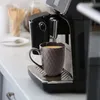 A close-up shot of a coffee mug filled with coffee, placed on the drip tray of a coffee machine. Produktbild-Vorschau