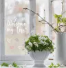 A window with a decorative text and flowers in a vase. Náhled obrázku produktu