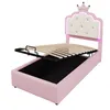 A pink upholstered bed frame with the mattress support raised, revealing storage space underneath. The headboard is white and tufted, shaped like a crown with LED lighting. Produktbild-Vorschau