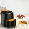 A black air fryer with French fries in its basket is on a countertop, with plates of food and berries nearby. Produktbild-Vorschau