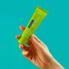 A hand holding a tube of toothpaste against a turquoise background. Anteprima dell’immagine prodotto