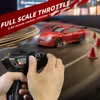 A person is holding a remote control for a red remote-controlled car that is drifting on a track with orange cones. Náhled obrázku produktu