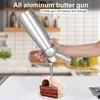 A hand holding a silver whipped cream dispenser over a slice of chocolate cake. Produktbild-Vorschau