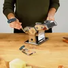 A person is shown operating a pasta maker on a wooden table. There are also ingredients like cheese and carrots on the table. Anteprima dell’immagine prodotto