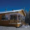A wooden cabin decorated with white icicle lights during winter. Voir les images du produit