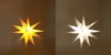 A split image showing two illuminated star-shaped lanterns, one with a warm yellow glow and the other with a bright white glow, against a neutral background. Voir les images du produit