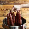 A hand is shown placing sausages on a rack inside a smoker. Produktbild-Vorschau