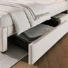 A close-up view of a beige upholstered bed frame with storage drawers pulled out, revealing folded grey blankets inside. Náhled obrázku produktu