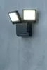A black LED floodlight with two adjustable heads is mounted on a textured gray wall. Podgląd zdjęcia produktu