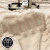 A close-up view of a thick, fluffy beige blanket, with a small graphic of a gift box in the lower-left corner. Anteprima dell’immagine prodotto