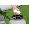 A hand is shown adding white filter balls to a pool filter system on a grassy surface. Produktbild-Vorschau