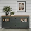 A dark green sideboard with a wooden top is displayed against a light gray paneled wall. Decorative items are placed on top and inside the sideboard. Podgląd zdjęcia produktu
