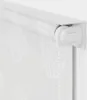 A close-up view of a white roller blind with a subtle seashell pattern, mounted on a white wall. Náhľad obrázku produktu