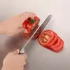 A person is slicing a tomato on a metal surface with a knife. Produktbild-Vorschau