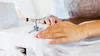 A close-up shot of a person's hands using a sewing machine to sew white fabric. Produktbild-Vorschau