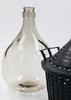 A clear glass carboy sits next to a black plastic basket, both on a white background. Produktbild-Vorschau