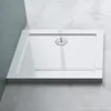 A white rectangular shower tray with a chrome drain is shown from a slightly elevated angle, resting on a concrete floor against a textured gray wall. Produktbild-Vorschau