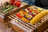 Two disposable grills with grilled vegetables and corn on a sunny outdoor setting. Produktbild-Vorschau