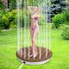 A woman is showering outdoors on a wooden platform in a garden. Náhled obrázku produktu