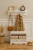 A hallway or entryway scene featuring a bench with storage, a coat, a handbag, and decorative items. Produktbild-Vorschau