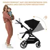 A woman holding a baby stands next to a stroller, with arrows indicating adjustments to the stroller's canopy and handle. Produktbild-Vorschau