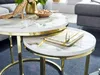 A close-up view of two nesting coffee tables with marble-look tops and gold metal frames, featuring a notebook and pen on the smaller table. Produktbild-Vorschau