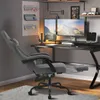 A grey gaming chair is set up next to a desk with dual monitors, keyboards, and speakers in a home office or gaming room setting. Produktbild-Vorschau