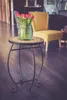 A small round table with a bouquet of red tulips in a glass jar sits on a wooden floor. A yellow chair is in the background. Produktbild-Vorschau