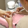 A person is getting their nails done at a nail salon, with a pink nail dust collector visible on the table. Anteprima dell’immagine prodotto