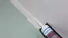 A close-up of a caulking gun applying white sealant to a corner joint between two walls. Produktbild-Vorschau