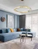 A modern living room with a large blue sectional sofa, a circular crystal chandelier, and a coffee table. Produktbild-Vorschau