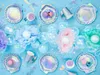 A collection of mermaid-themed party supplies arranged on a blue background. Produktbild-Vorschau