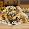 Three stuffed animal wild cats (tiger, leopard, and lion cub) are playfully interacting on a wooden surface with a newspaper underneath. Náhled obrázku produktu