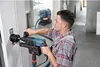 A man is using a Bosch rotary hammer with a dust extraction system attached to drill a hole in a concrete wall. A Bosch vacuum cleaner is visible in the background. Náhled obrázku produktu