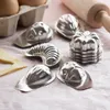A collection of metal baking molds arranged on a pink cloth surface, with eggs and a rolling pin in the background. Voir les images du produit