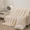 A cream-colored sherpa blanket is draped over a sofa, with two matching pillows in the foreground. Podgląd zdjęcia produktu