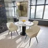 A dining set with a round table and four chairs in a well-lit room with large windows. Produktbild-Vorschau