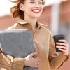 A woman is walking outdoors, holding a laptop bag and a coffee cup. Náhled obrázku produktu