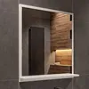 A bathroom mirror with a shelf, reflecting a tiled wall and wooden accents. Produktbild-Vorschau