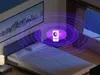 A mosquito repellent lamp is shown in a bedroom, emitting purple light waves. Produktbild-Vorschau