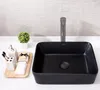 A black ceramic washbasin is displayed on a white countertop with various bathroom accessories. Náhľad obrázku produktu